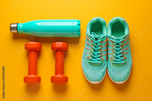 Sport shoes, bottle of water and dumbbells on color background