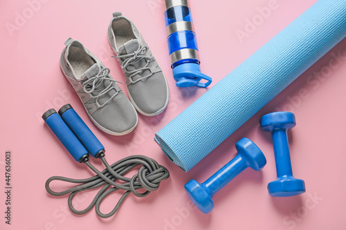 Sport shoes, yoga mat, bottle of water, dumbbells and skipping rope on color background