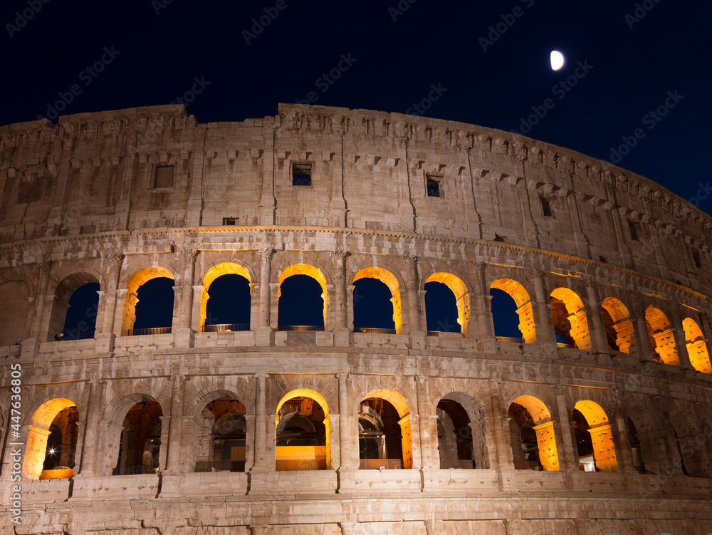 View of the ruins of the Roman Colosseum against the dark blue moonlit night sky. Rome, Italy