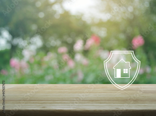 House with shield flat icon on wooden table over blur pink flower and tree in garden, Business home insurance and security concept