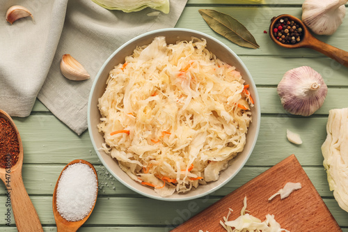 Bowl with tasty sauerkraut and ingredients on color wooden background