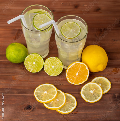 Two refreshing glasses of cold fruit juice with straw, ice lime and lemon juice, decorating with fresh lime and lemon on wooden table. Concept for refreshing