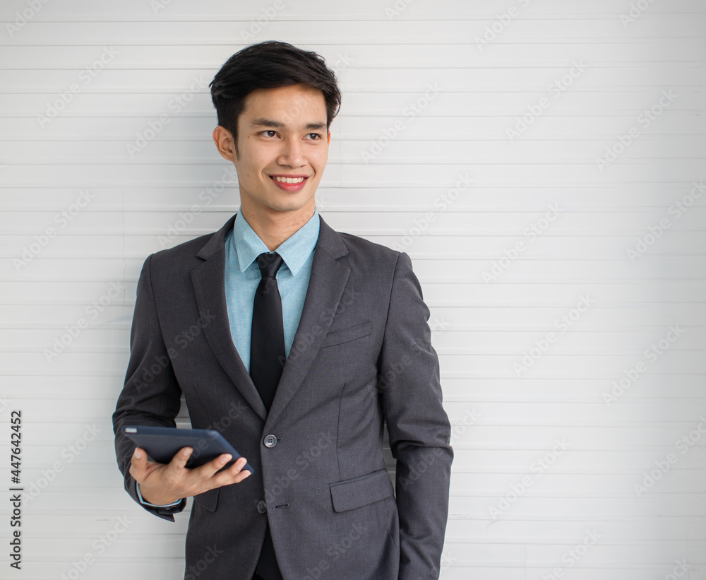 Young Asian businessman with tablet near gray wall Young Asian businessman with tablet near gray wall