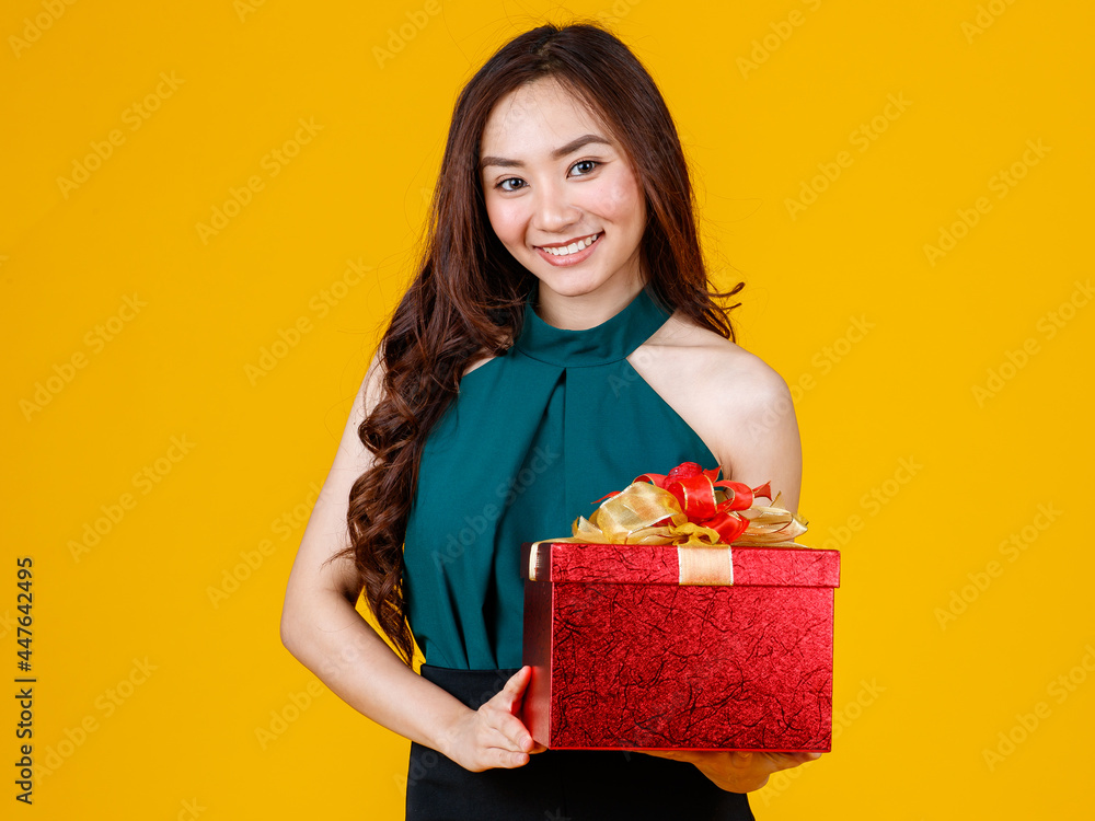 Happy smile face cute Asian girl with dark hair holding gift box with delightful and excited, studio shot on yellow background. Celebrate and festival concept.