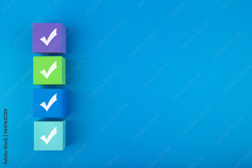 Creative flat lay with multicolored toy blocks with checkmarks on blue background with copy space. Concept of questionary, checklist, to do list, planning or business