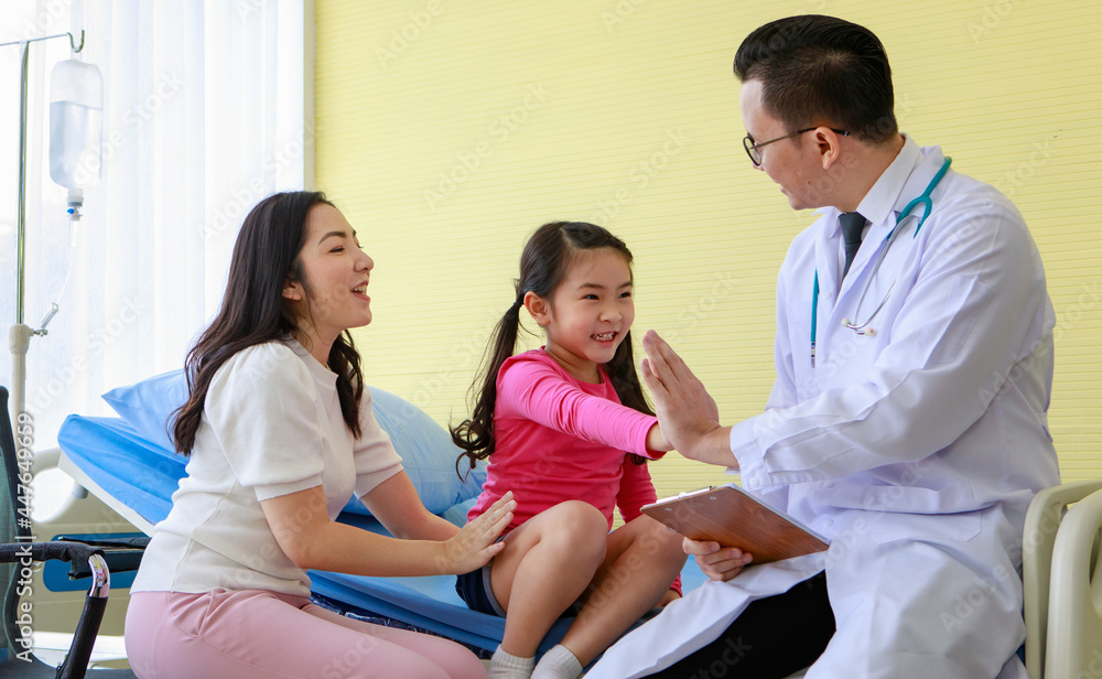 Cute and adorable Asian little girl sitting on patient bed in hospital and hi-five hand touching with doctor to compromise that she will surely get well after cure process Cute and adorable Asian little girl sitting on patient bed in hospital and hi-five hand touching with doctor to compromise that she will surely get well after cure process