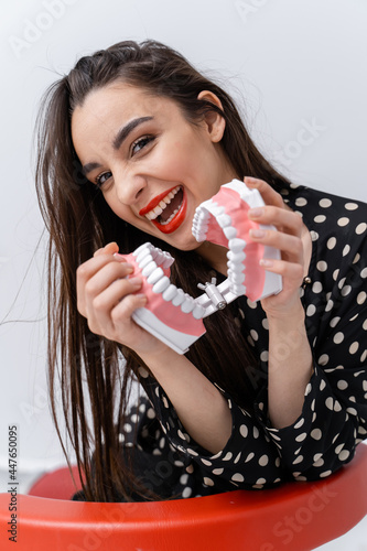 Waist up portrait view of the smile attractive woman with denture. Beautiful young female showing teeth  smiling while holding teeth model
