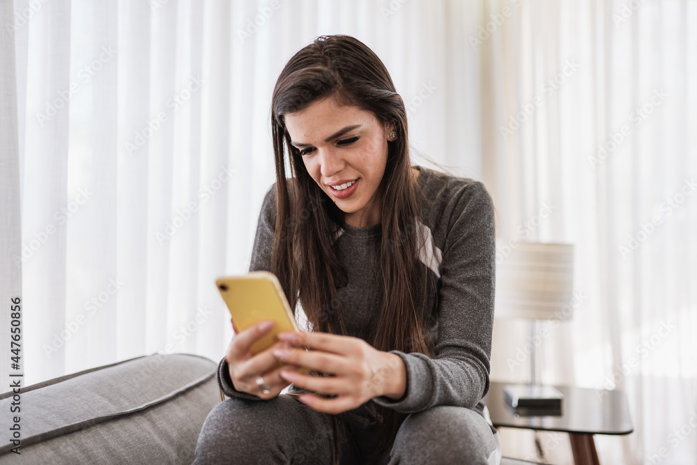 Happy Latin lady relax at home alone sit on room pose share good news at social media via cellphone. Smiling mixed race woman enjoy weekend order goods food online in phone app. Home office. Happy Latin lady relax at home alone sit on room pose share good news at social media via cellphone. Smiling mixed race woman enjoy weekend order goods food online in phone app. Home office.