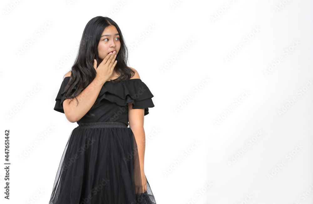 Horizontal portrait shot of an attractive young girl teenager standing and looking to copy space at the side of the image with raising hand up to close the mouth. Concept of unbelievable promotion