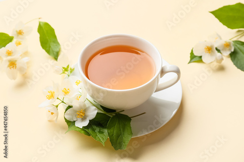 Cup of jasmine tea and flowers on color background