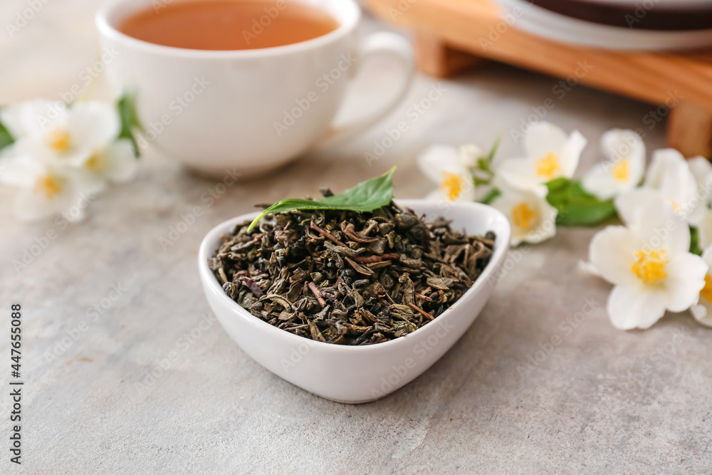 Bowl with dry green tea and cup of hot beverage on grunge background Bowl with dry green tea and cup of hot beverage on grunge background