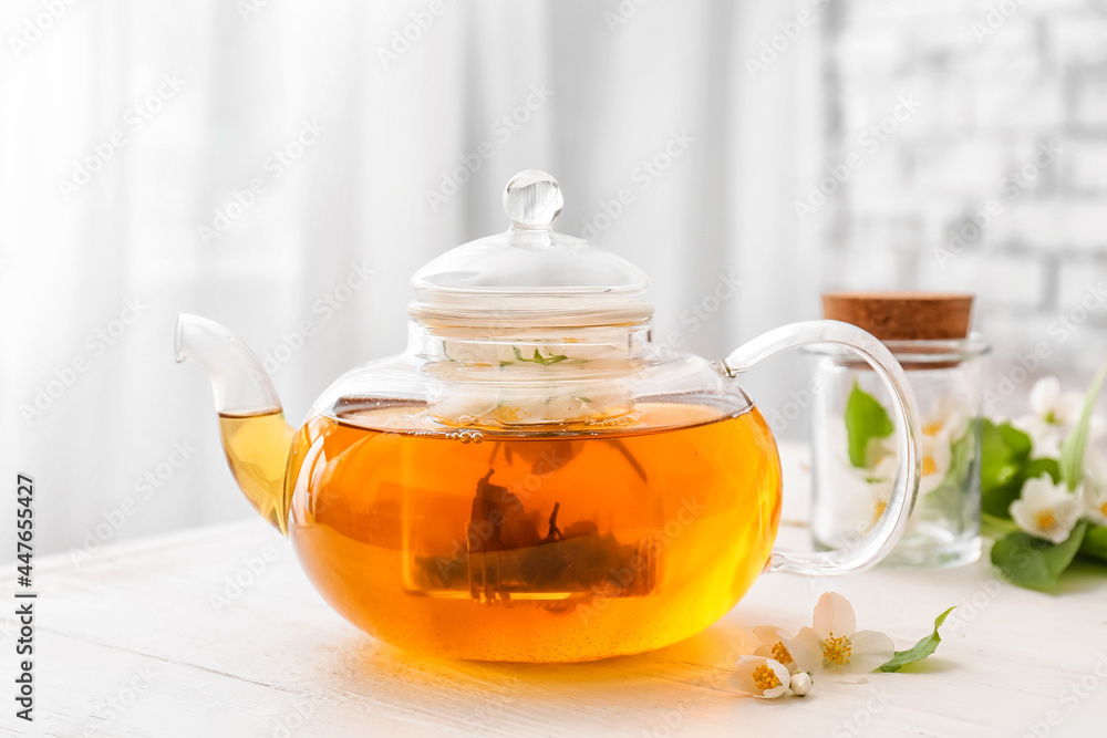 Teapot with aromatic jasmine tea and flowers on table in room Teapot with aromatic jasmine tea and flowers on table in room