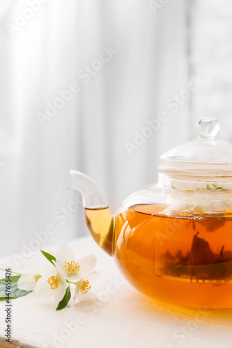 Teapot with aromatic jasmine tea and flowers on table in room