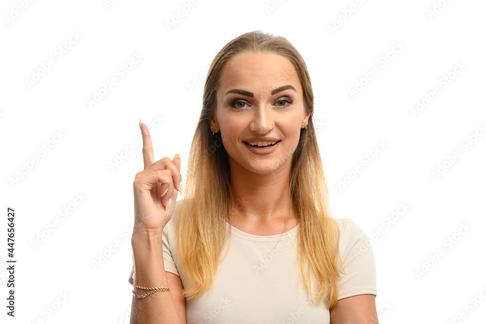 Portrait of a cute caucasian model girl in a white t-shirt smiling holding her finger up while looking at the camera on a white isolated background Portrait of a cute caucasian model girl in a white t-shirt smiling holding her finger up while looking at the camera on a white isolated background