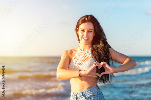 Fototapeta Naklejka Na Ścianę i Meble -  Young woman making heart symbol with hands sun blue sky background.Beautiful girl showing heart sign by hands