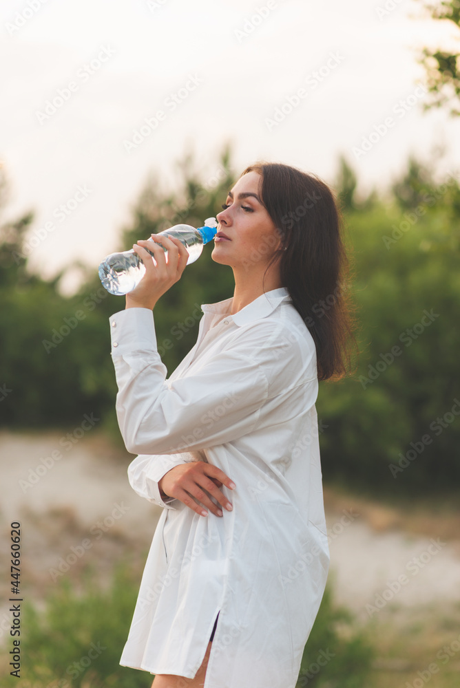 Girl drinks water from a plastic bottle.young caucasian woman in nature forest in woods while holding bottle of water Girl drinks water from a plastic bottle.young caucasian woman in nature forest in woods while holding bottle of water