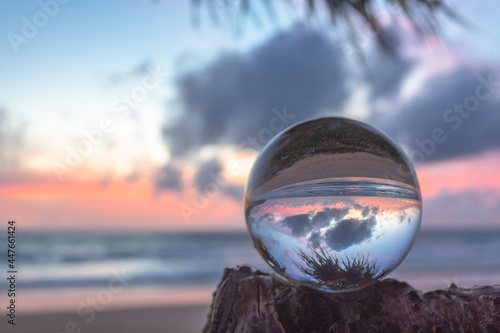 beautiful cloud moving and red sunset inside crystal ball placed on a branch beside the beach. Unique and creative travel and nature idea. © Narong Niemhom