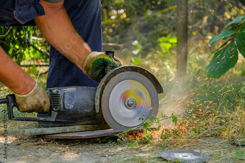 A circular saw in the hands of a worker cuts metal with an abrasive disc. Sparks and metal shavings fly around.