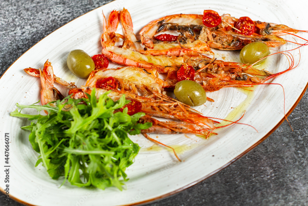 Fried langoustines served with olives and salad leaves. Grilled tasty langoustines on a white oval plate. Restaurant serving, horizontal orientation. Fried langoustines served with olives and salad leaves. Grilled tasty langoustines on a white oval plate. Restaurant serving, horizontal orientation.