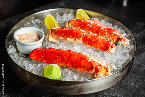 Phalanxes of red crab on ice. Lies on ice with lemon and lime and sauce. Restaurant serving. Low key, dark background, horizontal orientation