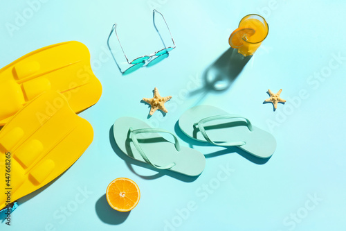 Flip-flops, sunglasses, flippers and glass of juice on color background