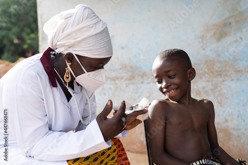 Black nurse with face mask injecting a dose of vaccine to a smiling brave schoolboy in an African hospital setting photo