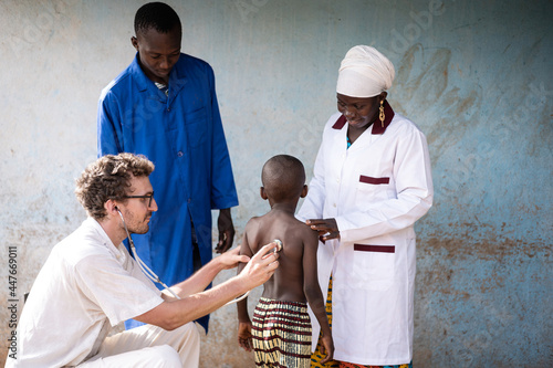 Schilderij op canvas White medical volunteer auscultating the lungs of a skinny little African boy un