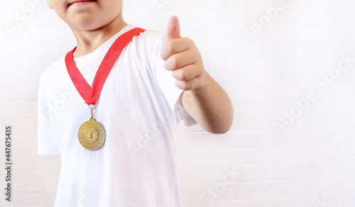 A happy teenage boy-dressed in a gold medal, smiles and gives a thumbs up to the camera, standing isolated against a white background. selective focus. the concept of sports and victories