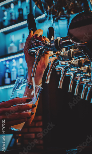 woman bartender hand at beer tap pouring a draught beer in glass serving in a restaurant or pub