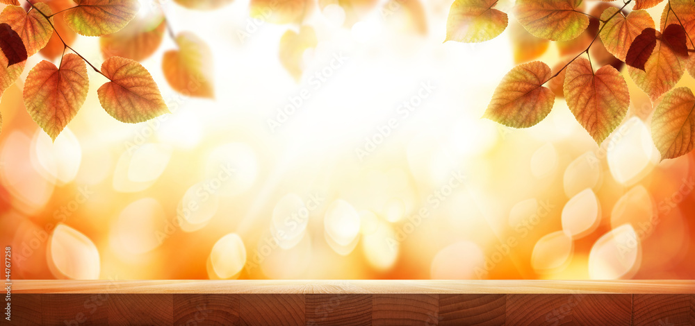A wood table, tabletop product display with a golden autumn sunset sky and leaf background for seasonal, autumnal thanksgiving images.
