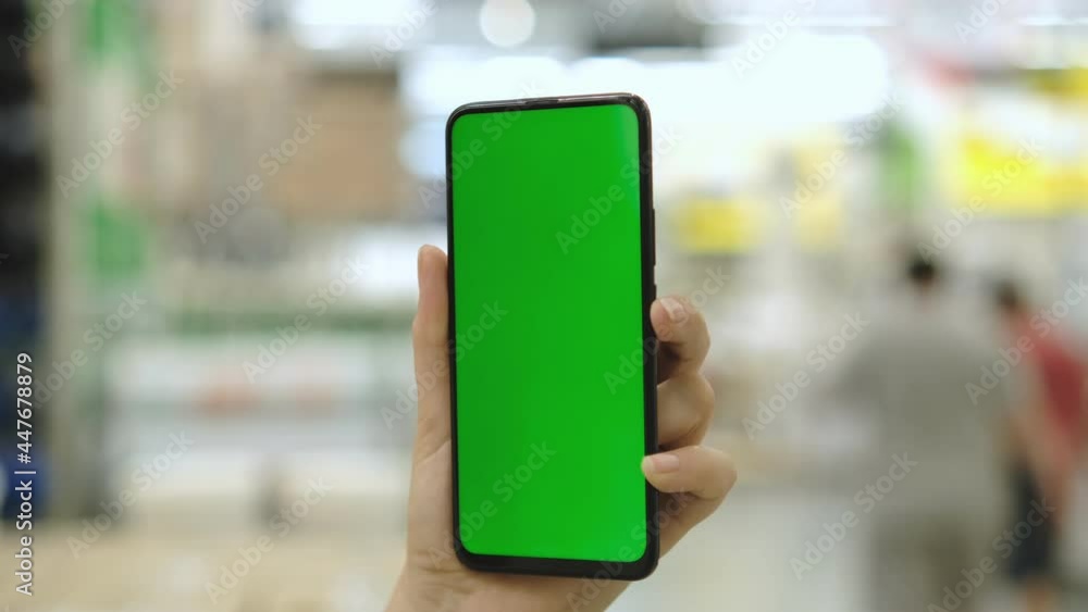 Shopping center. Mall. Department store. Back view of brunette holding chroma key green screen smartphone watching content. Shopping online. Gadgets and contemporary people concept. Shopping center. Mall. Department store. Back view of brunette holding chroma key green screen smartphone watching content. Shopping online. Gadgets and contemporary people concept.