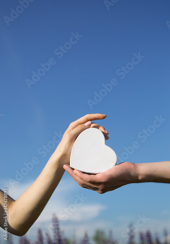 concept of love, support, hope, health care. male and female hands holding a white heart on a background of blue sky. World heart day. Copy space