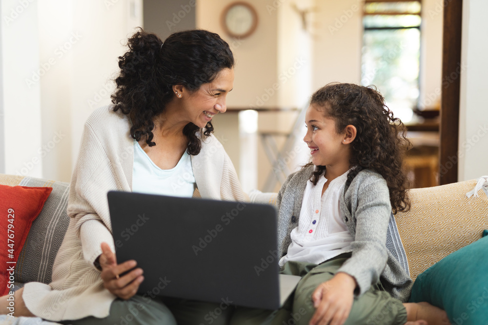 Smiling mixed race mother and daughter sitting on sofa and using laptop Smiling mixed race mother and daughter sitting on sofa and using laptop