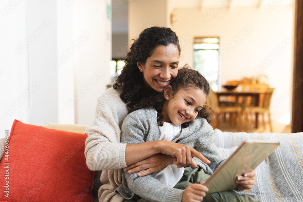 Smiling mixed race mother and daughter sitting on sofa, using tablet Smiling mixed race mother and daughter sitting on sofa, using tablet