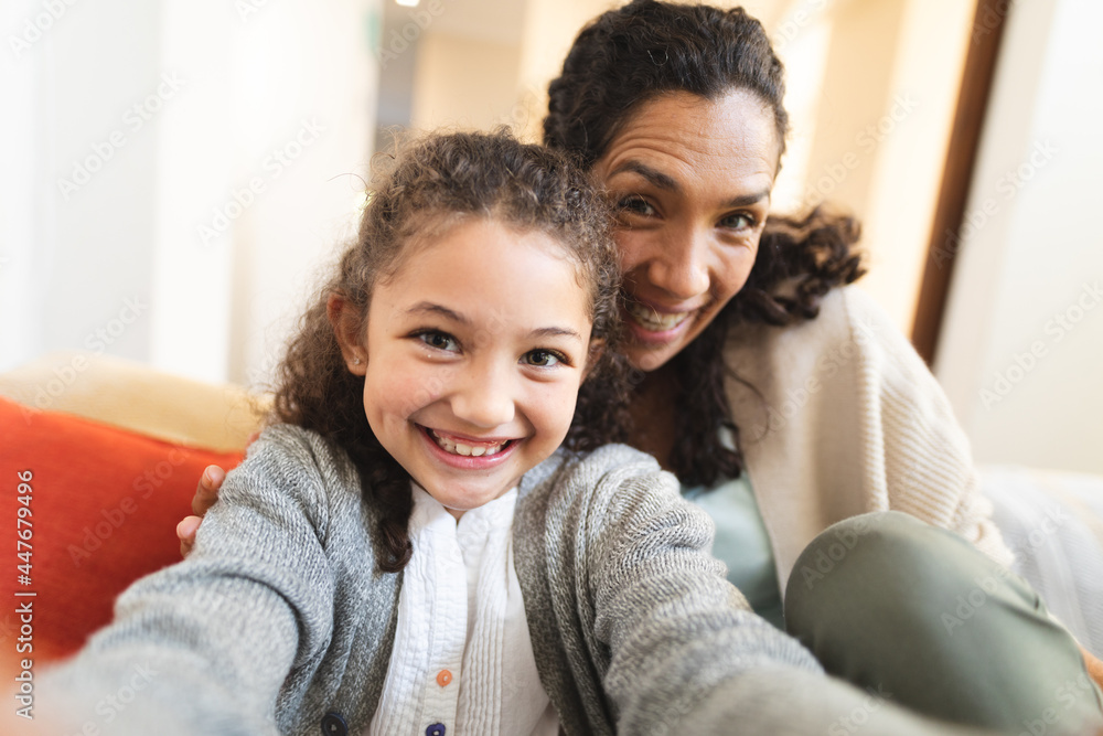 Mixed race mother and daughter sitting on sofa doing funny faces, taking selfie Mixed race mother and daughter sitting on sofa doing funny faces, taking selfie