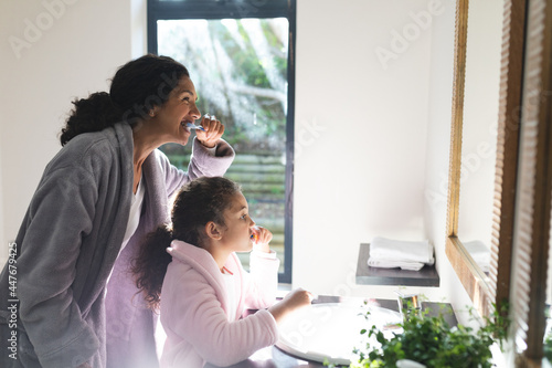 Midsection of mixed race mother and daughter brushing teeth in bathroom