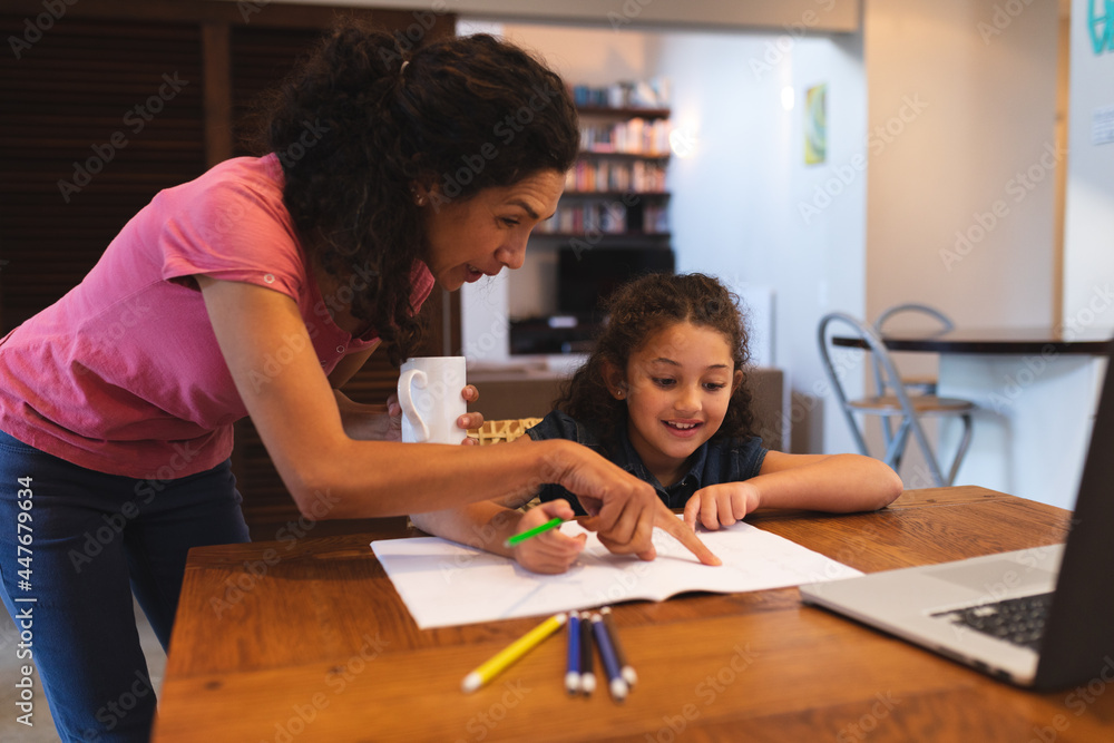 Mixed race mother holding coffee, helping her daughter do homework Mixed race mother holding coffee, helping her daughter do homework