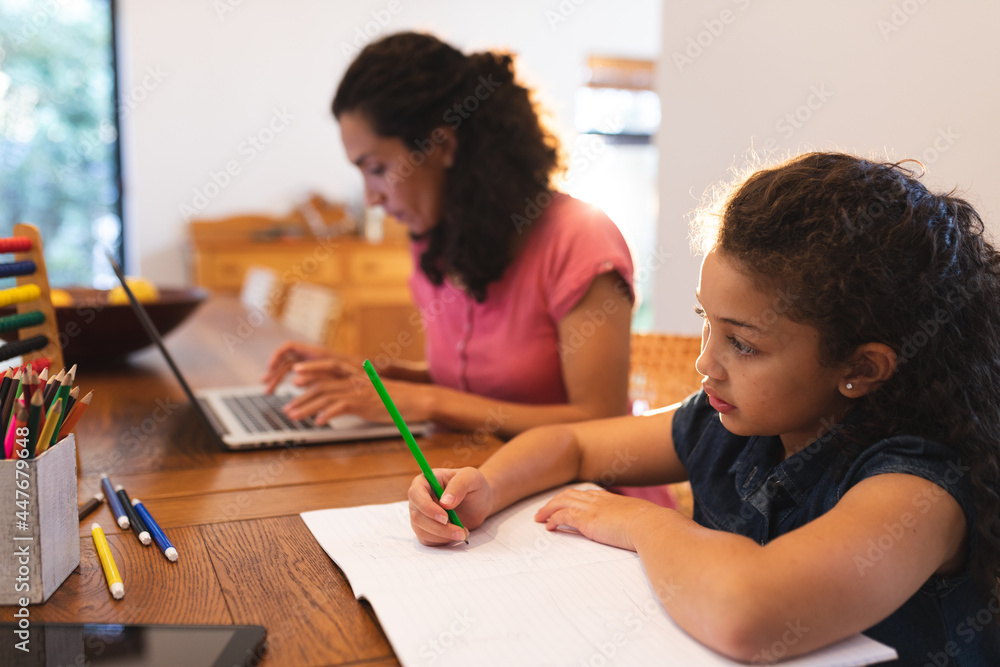 Mixed race mother and daughter sitting at table, working on laptop and drawing Mixed race mother and daughter sitting at table, working on laptop and drawing