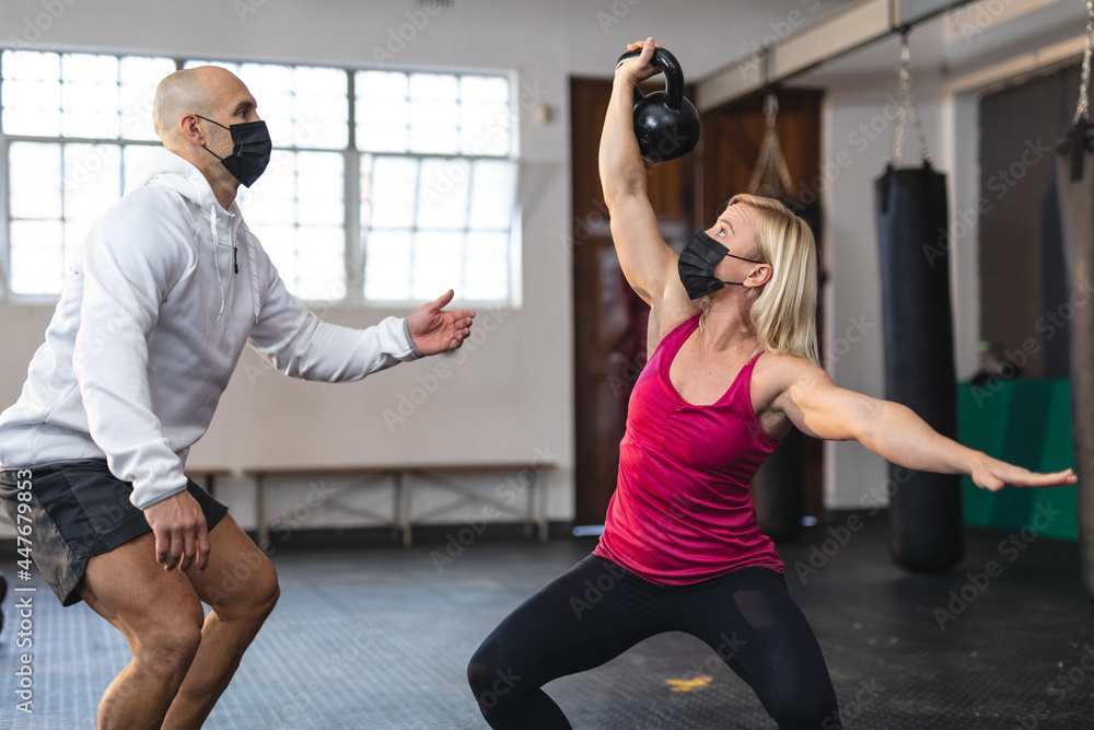 Caucasian male trainer instructing woman exercising at gym wearing face masks, lifting weights Caucasian male trainer instructing woman exercising at gym wearing face masks, lifting weights