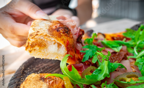 woman Hand takes a slice of meat neapolitan Pizza with Mozzarella cheese, ham, bacon, tomato, Spices and jalapeno in cafe outdoor