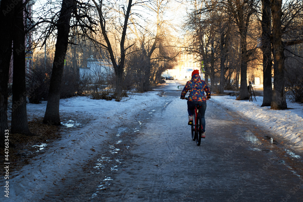 A girl in bright clothes rides a mountain bike in bad weather. Winter or early spring, snowy and wet road. Opening a cycling season or using a bicycle as transport at any time of the year.