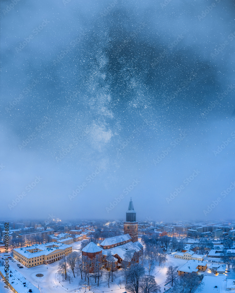 Aerial of Turku city center and the Cathedral in at night in Finland with an epic milky way on the sky between the clouds. Artistic cityscape image.