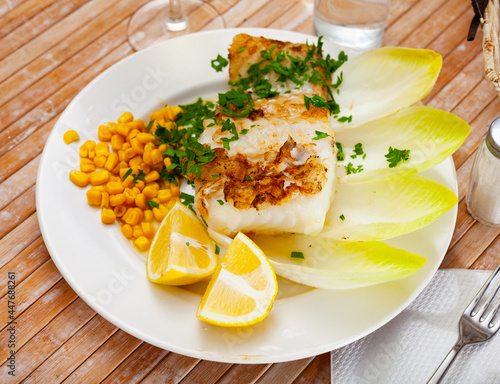 Appetizing fried rockling fillet with garnish of boiled corn seeds, lemon slices and fresh greens photo