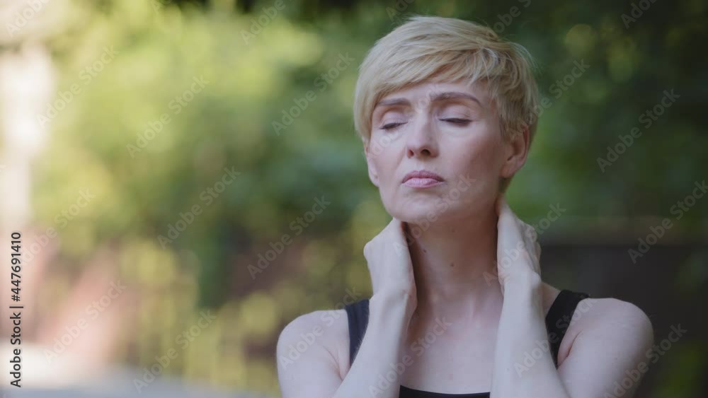 Outdoors portrait sad upset middle aged caucasian woman athlete stands in city park feels pain in neck suffers from painful symptoms of arthritis sores damage muscle problems spasm massages shoulders Outdoors portrait sad upset middle aged caucasian woman athlete stands in city park feels pain in neck suffers from painful symptoms of arthritis sores damage muscle problems spasm massages shoulders