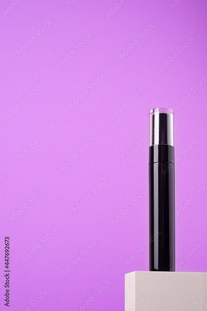 Black mascara tube with a transparent cover on a white podium and purple background. Makeup product for eyes with space for text. Black mascara tube with a transparent cover on a white podium and purple background. Makeup product for eyes with space for text.