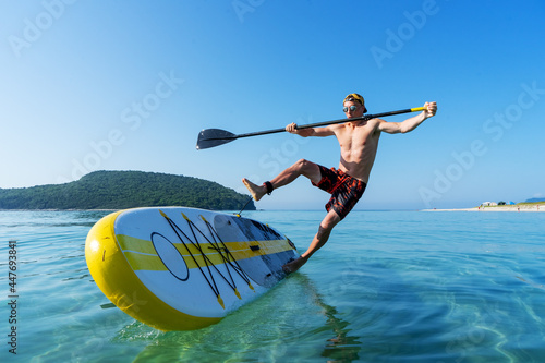 A man learns to stand on a board and falls into the water from a large yellow paddle board. photo