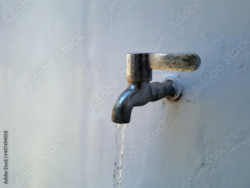 Water flows from stainless steel water taps mounted on white concrete walls in an urban house in the morning