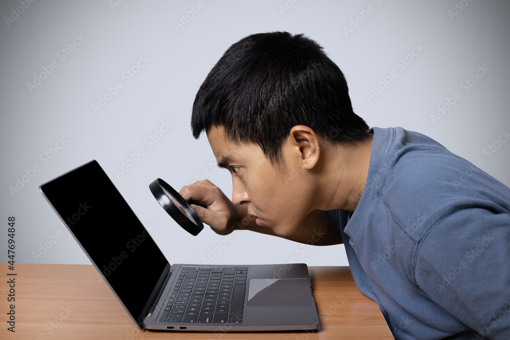 Young man observing laptop with magnifying glass isolated on gray background. Young man observing laptop with magnifying glass isolated on gray background.
