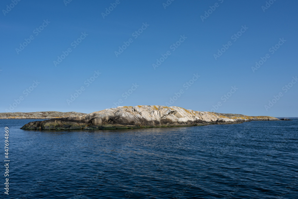A picture of a beautiful rock island. Ocean and blue sky in the background. Picture from the Weather Islands, on the Swedish West coast