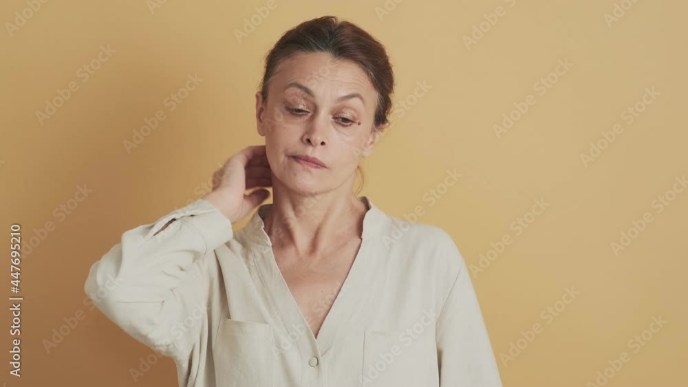 A confused middle-aged brunette woman shrugging shoulders standing isolated over beige background in the studio A confused middle-aged brunette woman shrugging shoulders standing isolated over beige background in the studio